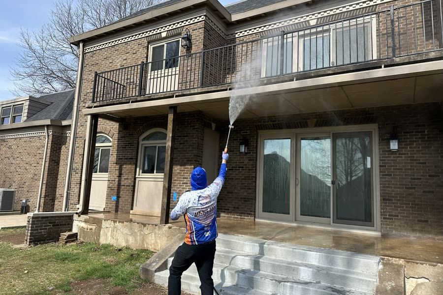 Worker spraying the underside of a balcony on a two-story brick home