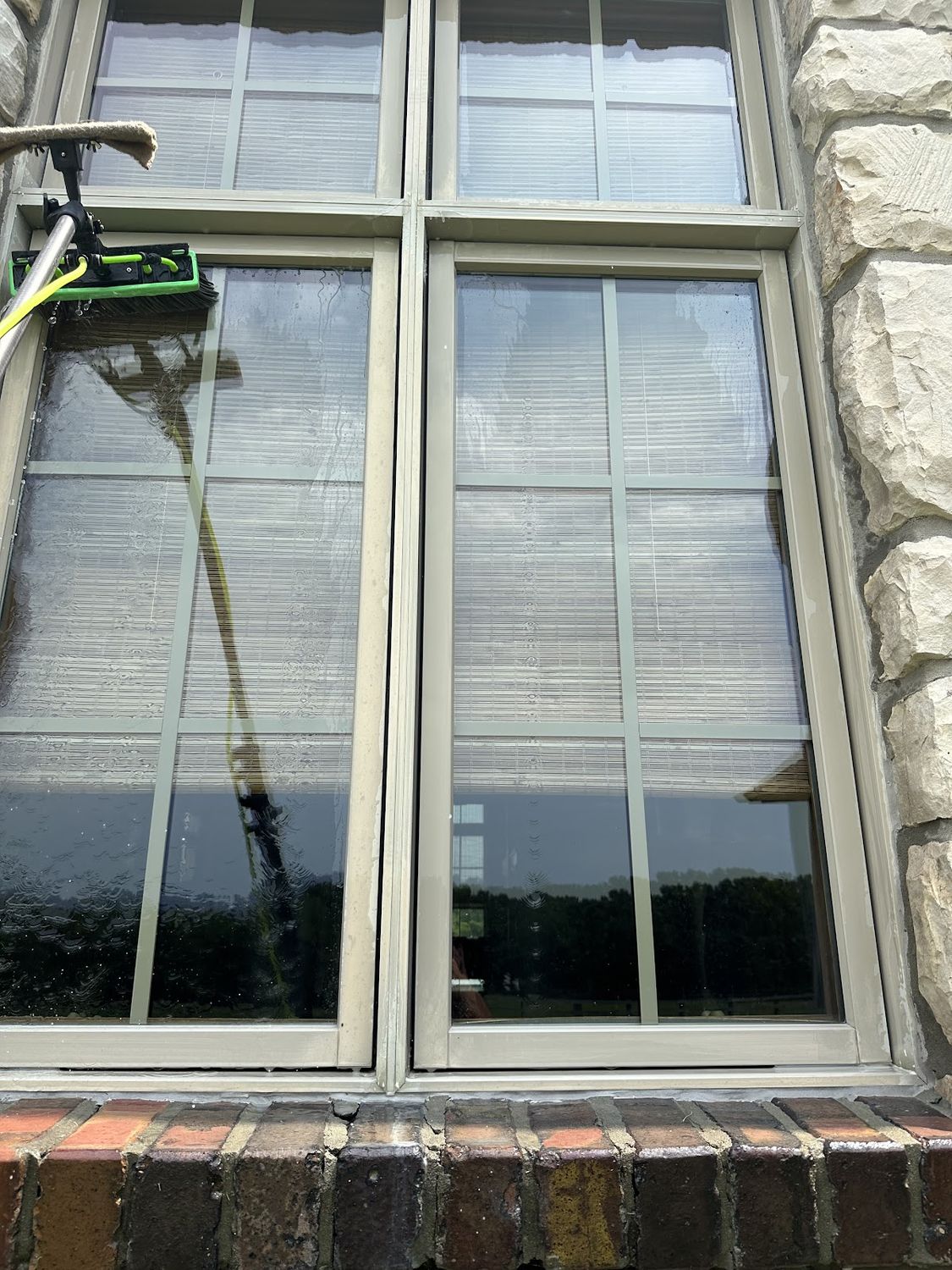 Water-fed pole brush cleaning a tall window on a stone home in Springfield MO, water running down the glass