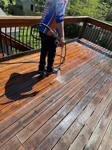 Worker pressure washing a wooden deck part-way across the boards