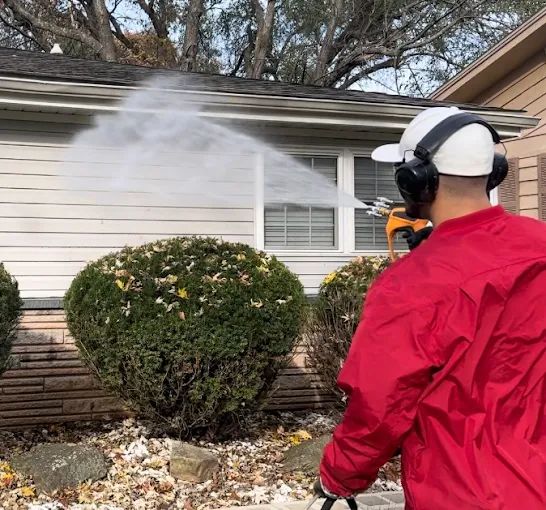 Worker spraying the siding of a single-story home with a low-pressure soft washing solution