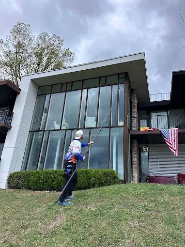 Worker cleaning the tall glass wall of a modern angular home with a water-fed pole