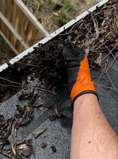 Gloved hand scooping packed leaves and grit out of a gutter